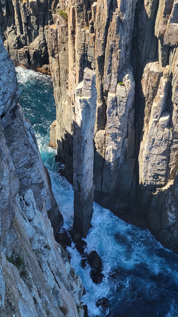 A dramatic vertical dolerite sea stack known as the Totem Pole, standing tall in the turquoise ocean at Cape Hauy on the Tasman Peninsula, Tasmania.
