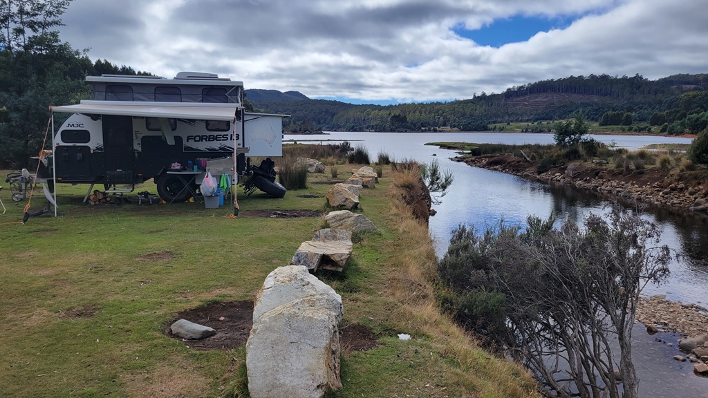 Off-grid free camping at Lake Gairdner, Tasmania, showing a self-contained caravan setup near the water’s edge on a clear day.