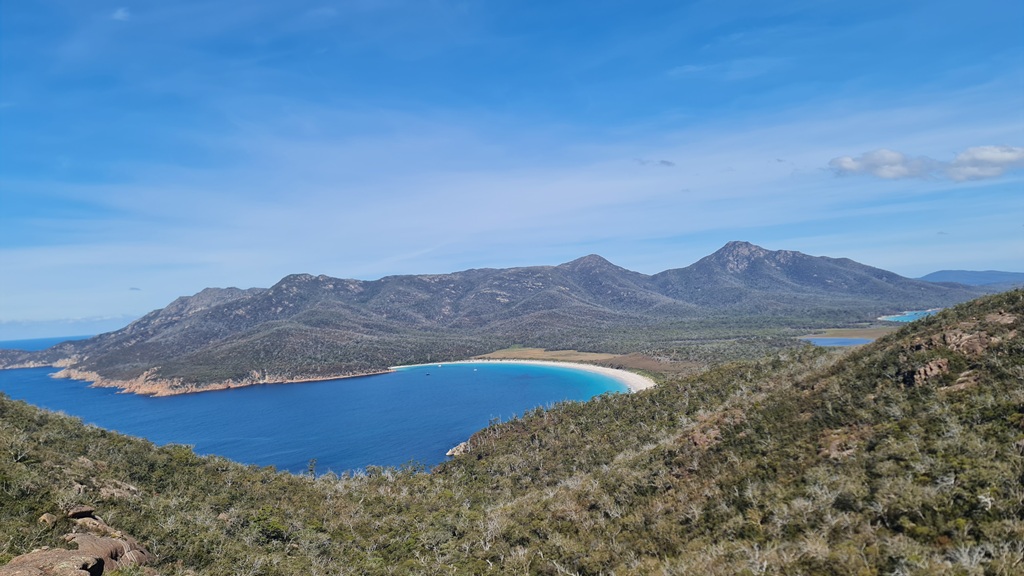 The iconic Wineglass Bay lookout view on Tasmania's East Coast, showing the white sand beach and azure ocean during a sunny day on the Great Eastern Drive.