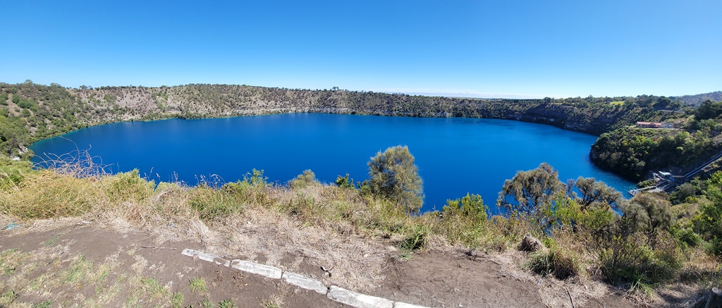 A wide panoramic view of the vibrant cobalt-blue water of the Blue Lake in Mount Gambier, a volcanic crater lake seen from a high lookout during a South Australia road trip under a clear, bright sky.