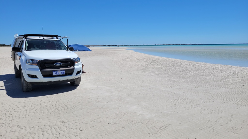 A white Ford Ranger parked on the expansive white sands of Flaherty's Beach during a Yorke Peninsula road trip, with shallow turquoise waters and sandbars stretching toward the horizon under a clear blue sky.