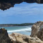 A view through a rugged limestone sea cave looking out toward the turquoise waves and coastal cliffs of Osmanli Beach, a scenic stop on a Kangaroo Island itinerary