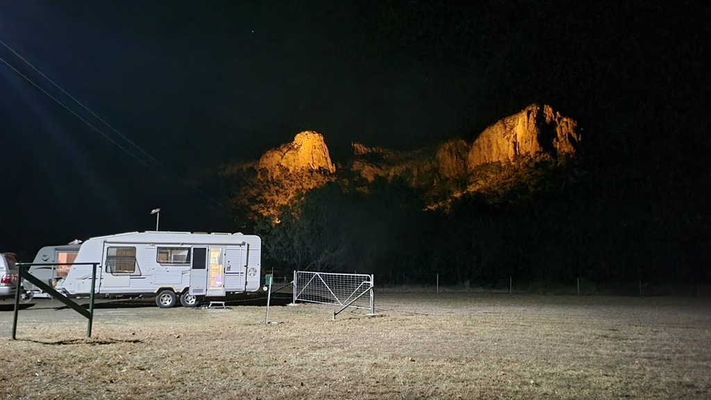 Caravan parked at Virgin Rock Free Camping Springsure Queensland at night with the massive illuminated limestone cliff face in the background