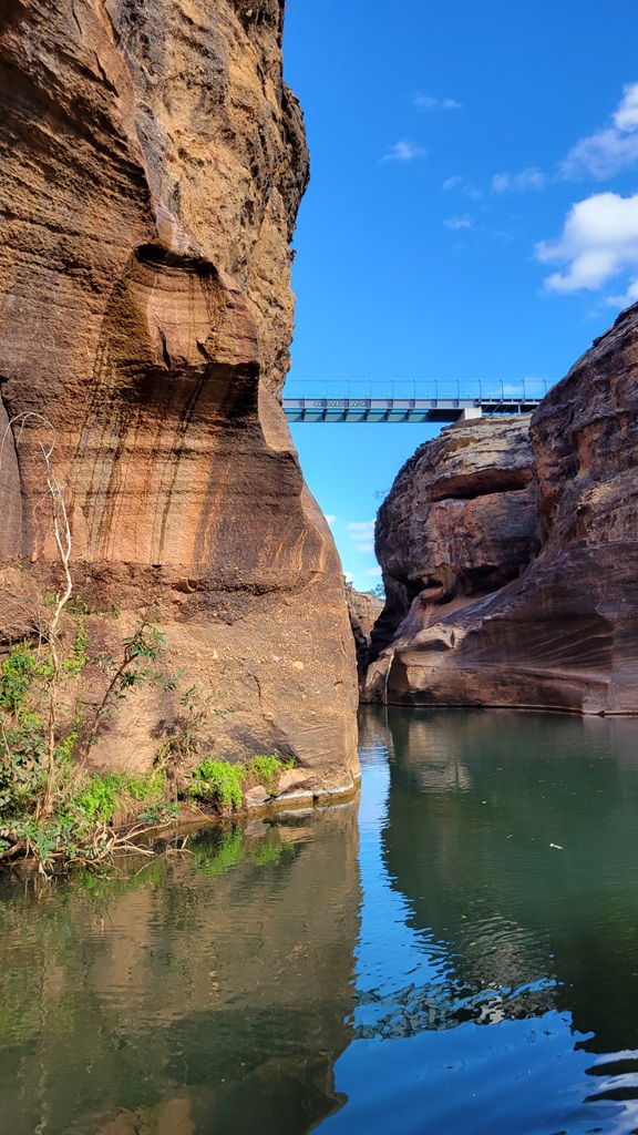 The glass-bottom pedestrian bridge spanning the narrow sandstone cliffs of Cobbold Gorge in outback Queensland, viewed from the calm water below.