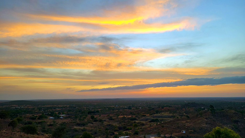 Vibrant sunset over the outback horizon from Towers Hill Lookout in Charters Towers, Queensland, featuring orange and gold clouds over a rugged inland landscape.