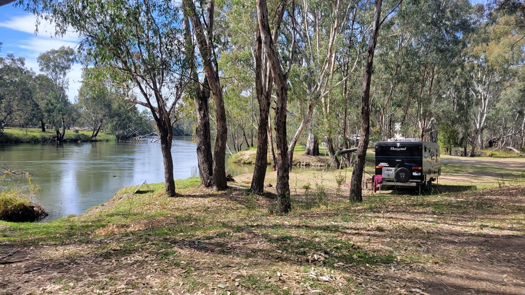 A caravan set up for free camping on a grassy bank right next to the river at Doolans Bend on the Murray River.