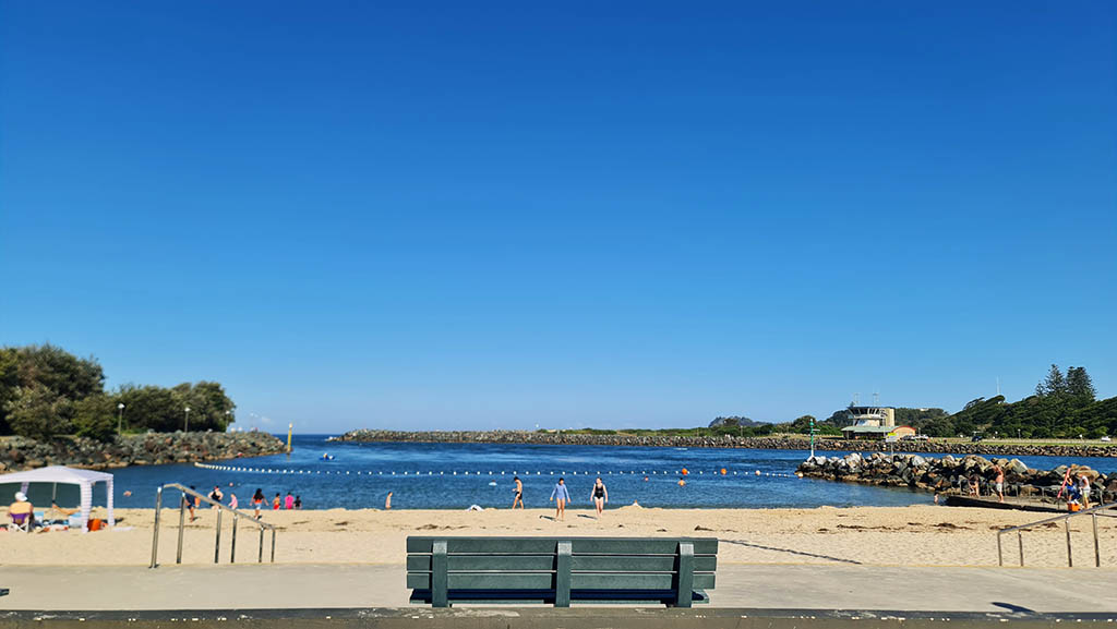 Park bench overlooking the sandy beach and calm swimming area at Tuncurry Rock Pool