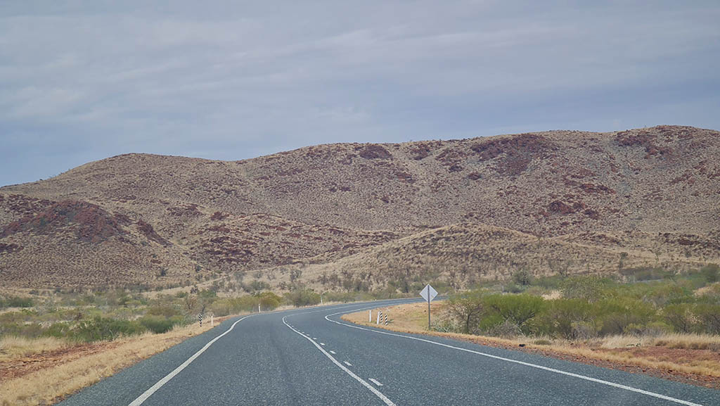 Sealed highway winding past spinifex-covered hills between Port Hedland and Karratha